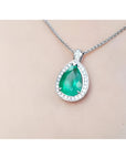 Pear-shaped emerald pendant with halo diamonds in 14K white gold, worn on a chain.