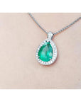 Pear-shaped emerald pendant with halo diamonds in 14K white gold, worn on a chain.
