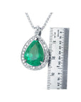 8.64 ct. pear-shaped emerald pendant with halo diamonds in 14K white gold, next to a ruler.