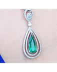 Teardrop-shaped emerald pendant with diamond accents on a person's chest.