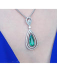 2.13 ct teardrop emerald pendant with double diamond halo, set in 18K white gold on a woman's neck.