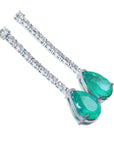 Pair of teardrop natural emerald earrings and diamond-studded clasps on a white background