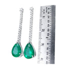 Pair of emerald teardrop earrings with white gold detailing next to a ruler for scale on a white background