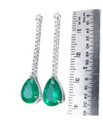 Pear shape 5.05 ct. emerald drop earrings in 18K white gold with diamond accents, shown with ruler.
