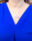 Person wearing a blue top with a butterfly pink agate pendant and silver necklace.
