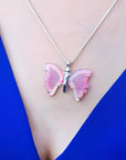 Pink natural agate butterfly pendant on a silver necklace, worn on a person in a blue top.