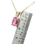 Gold necklace with a pink natural sapphire pendant next to a ruler for scale.