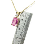Gold necklace with a pink natural sapphire pendant next to a ruler for scale.