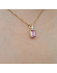14k solid gold necklace with a natural pink sapphire pendant on a person's neck.