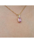14k solid gold necklace with a natural pink sapphire pendant on a person's neck.