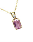 A natural emerald-cut pink sapphire and diamond pendant necklace in a prong setting, crafted in 14k yellow gold.