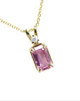 A natural emerald-cut pink sapphire and diamond pendant necklace in a prong setting, crafted in 14k yellow gold.