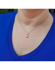 Person wearing a blue top with a 14k gold necklace featuring a pink sapphire pendant.