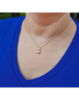 Person wearing a blue top with a 14k gold necklace featuring a pink sapphire pendant.