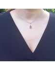 Teardrop-shaped pink sapphire gemstone necklace on a woman wearing a black dress.