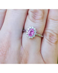 14K white gold ring with oval pink sapphire and diamond halo on a finger.