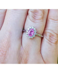 14K white gold ring with oval pink sapphire and diamond halo on a finger.