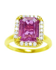 This pink sapphire ring for women showcases a sparkling, eye-clean emerald cut, surrounded by halo diamonds and set in 14k yellow gold.
