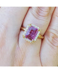 Emerald-cut pink sapphire ring with diamond halo in 14K yellow gold on a hand.