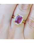 Emerald-cut pink sapphire ring with diamond halo in 14K yellow gold on a hand.