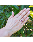 Hand wearing a pink sapphire gemstone ring with green foliage in the background