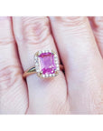 Pink sapphire ring for women emerald-cut halo diamonds 14k yellow gold, o a woman's hand.