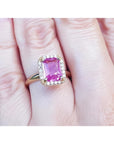 Pink sapphire ring for women emerald-cut halo diamonds 14k yellow gold, o a woman's hand.