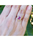 Emerald-cut pink sapphire ring with diamond halo in 14K yellow gold on a woman's hand.
