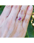 Emerald-cut pink sapphire ring with diamond halo in 14K yellow gold on a woman's hand.