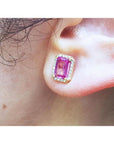 Pink sapphire emerald cut stud earring with diamond halo in 14K yellow gold on an ear.