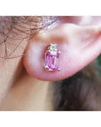 Close-up of an ear wearing a pink natural sapphire earring with a blurred background