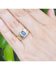 Gold ring with a blue sapphire gemstone on a hand against a green leafy background