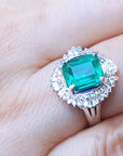A platinum emerald ring with diamond halo on a hand.