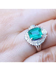 A platinum emerald ring with diamond halo on a hand.