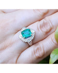 Emerald ring with diamond halo on a hand.