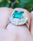 Ring with a Muzo emerald and diamond accents on a finger against a blurred natural background.