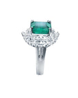 Ring with a colombian emerald and diamond-studded band on a white background.