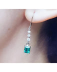 A natural Muzo colombian emerald dangle earring in white gold on an ear lobe.