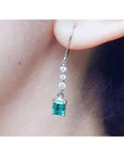 A natural Muzo colombian emerald dangle earring in white gold on an ear lobe.