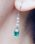 Close-up of a natural emerald dangle earring on an ear lobe.