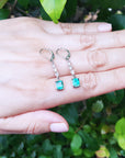 Pair of lever backs emerald dangle earrings held on a hand against a green leafy background