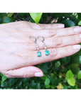 14K white gold dangle earrings with rectangular Colombian emeralds and clear stones on a hand.
