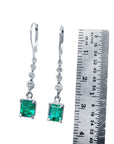 Pair of Colombian Emerald dangle earrings with a ruler for scale on a white background