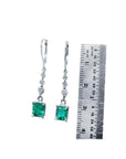 14K white gold dangle earrings with square-cut Colombian emeralds and diamond accents, next to a ruler.