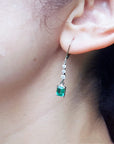 Close-up of an ear wearing a natural emerald earring with a blurred background