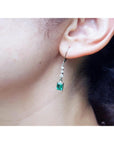 Close-up of an ear wearing a natural emerald earring with a blurred background