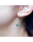 14K white gold dangle earrings with three small diamonds and a square-cut Colombian emerald.