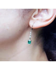 14K white gold dangle earrings with three small diamonds and a square-cut Colombian emerald.