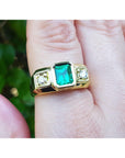 Gold ring with a square natural emerald on a finger against a blurred natural background.