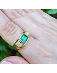 Gold ring for men with emerald and diamonds on a finger against a natural background.